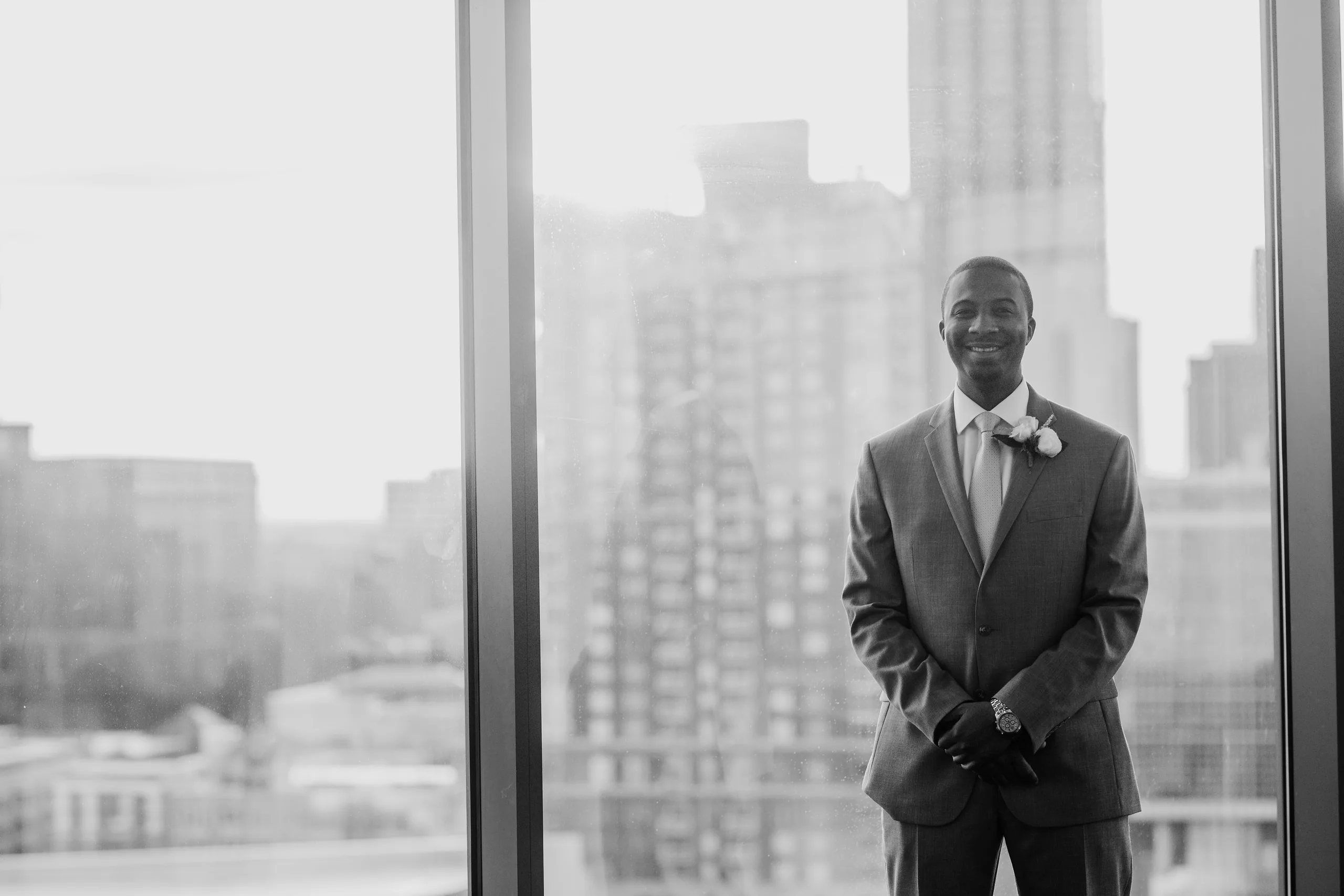 Getting Ready: the groom at the window above downtown, in black and white, before their elopement at Ventanas in Atlanta, GA