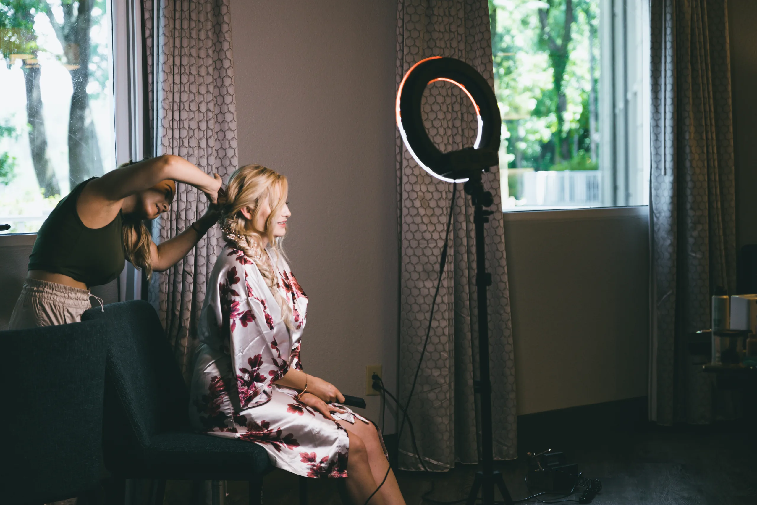 Getting Ready: the bride having her hair done by the window in her floral robe, before their wedding at Atlanta Evergreen Lakeside Resort in Stone Mountain, GA