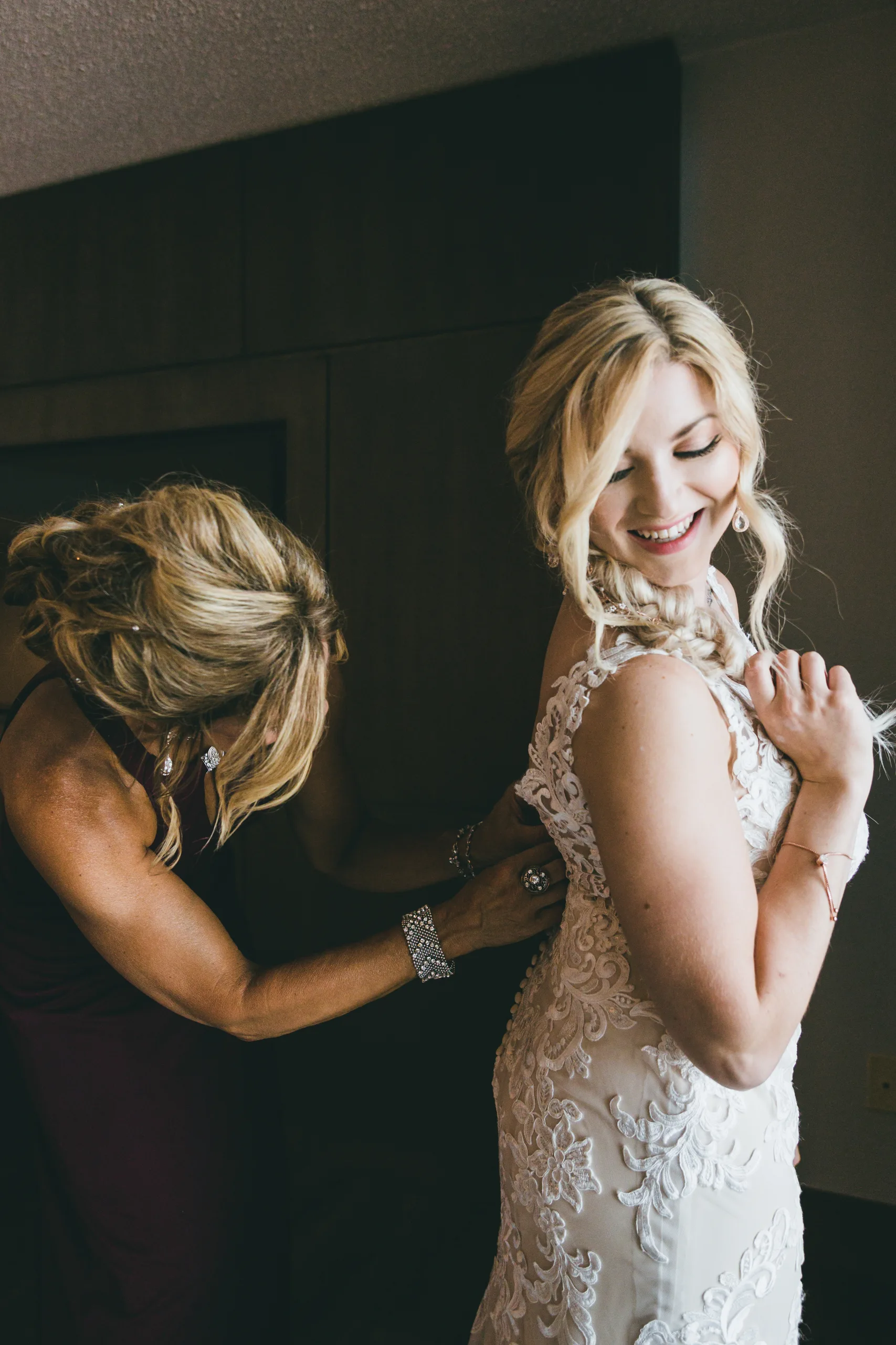 Getting Ready: the bride smiling over her shoulder as her mom buttons her gown, before their wedding at Atlanta Evergreen Lakeside Resort in Stone Mountain, GA
