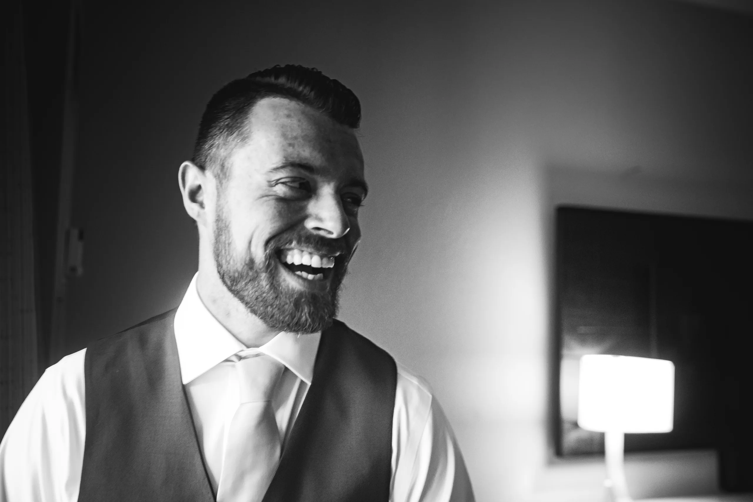 Getting Ready: the groom laughing, in black and white, before their wedding at Atlanta Evergreen Lakeside Resort in Stone Mountain, GA