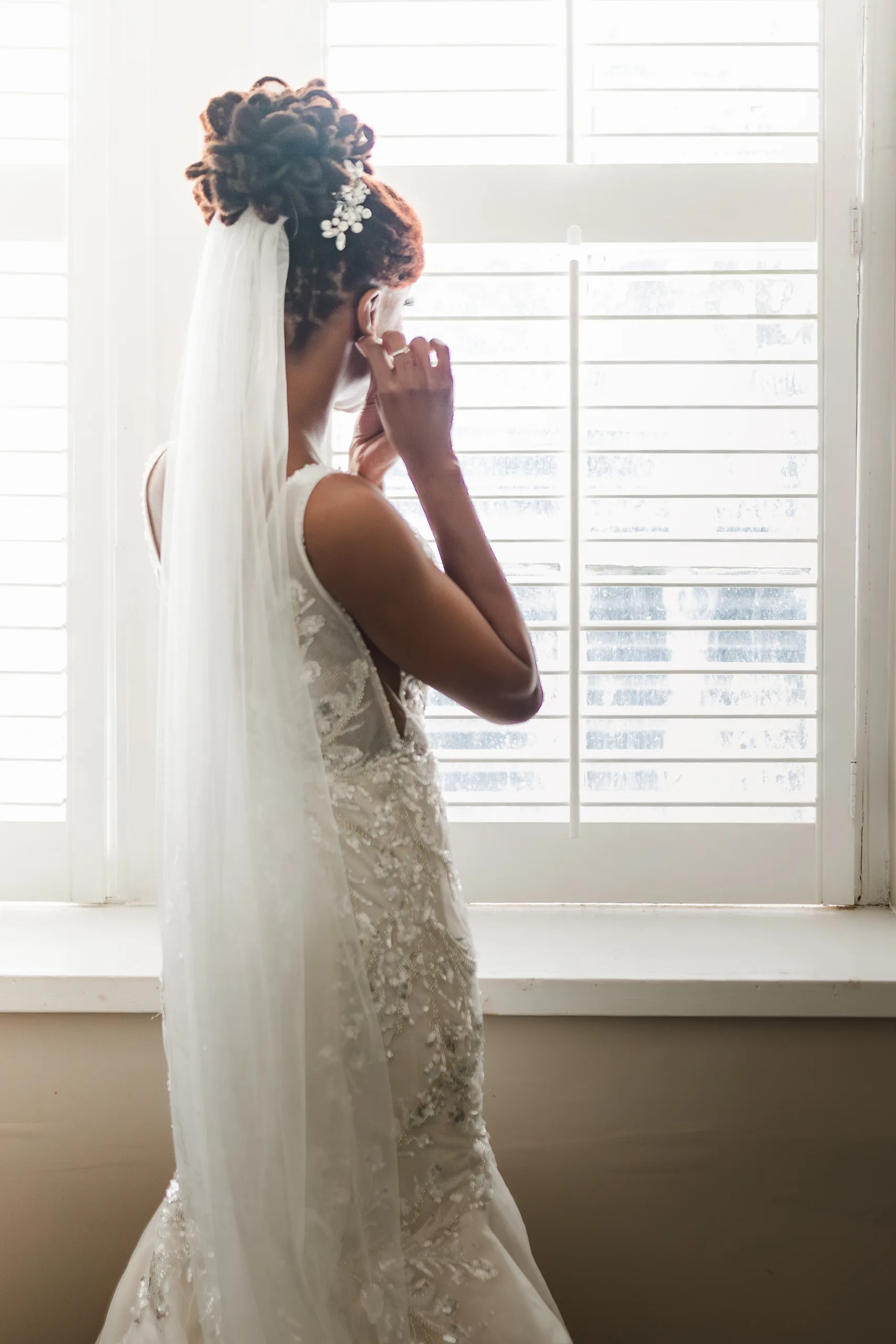 Getting Ready: the bride putting in her earring at the window, before their wedding at the Historic DeKalb Courthouse in Decatur, GA