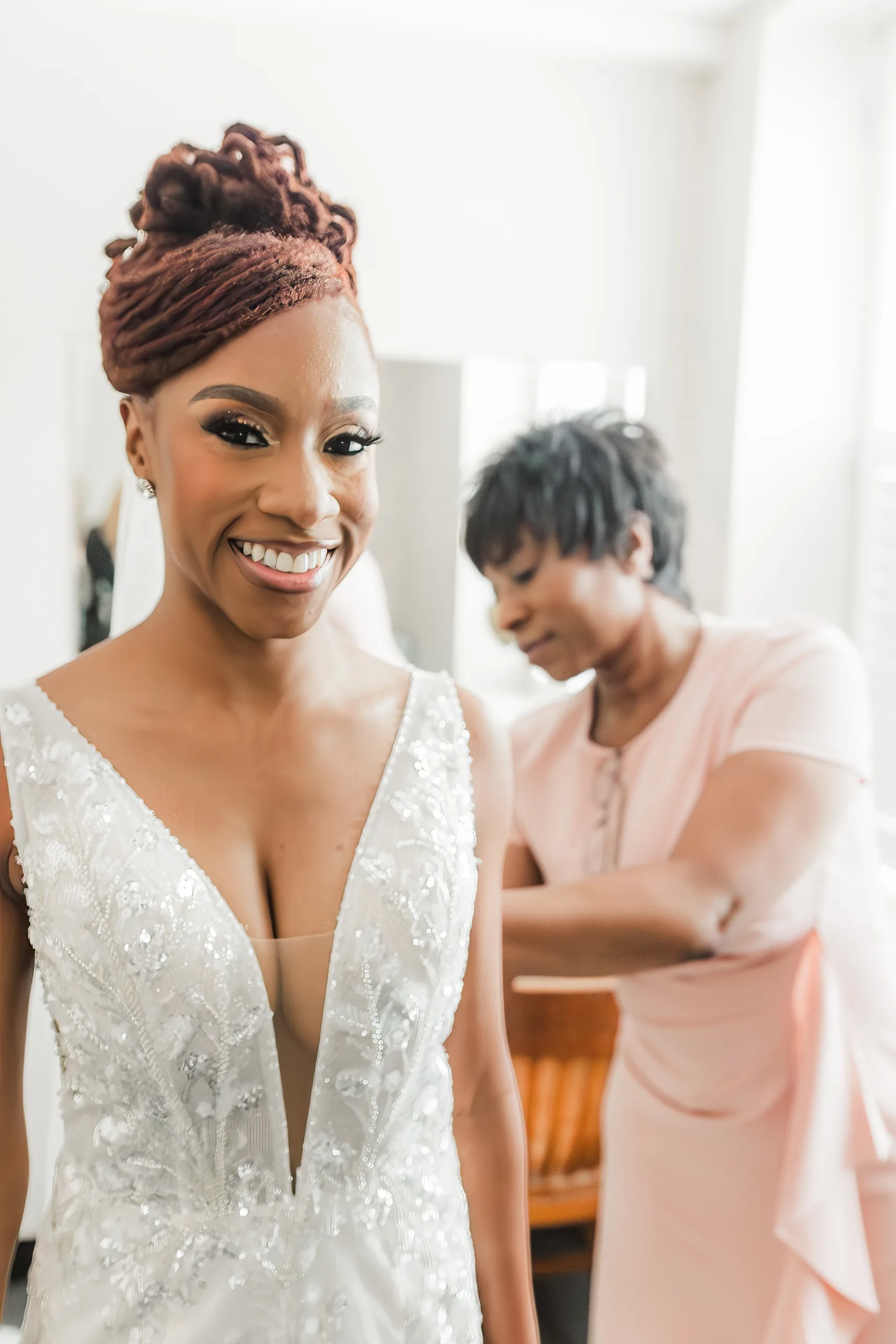 Getting Ready: the bride smiling as she is buttoned into her gown, before their wedding at the Historic DeKalb Courthouse in Decatur, GA