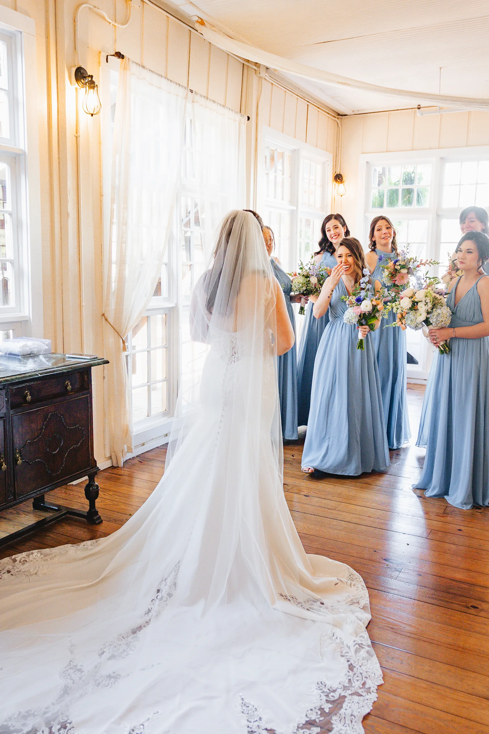Getting Ready: her bridesmaids in dusty blue seeing her for the first time before their wedding at Ivy Hall at Roswell Mill in Roswell, GA