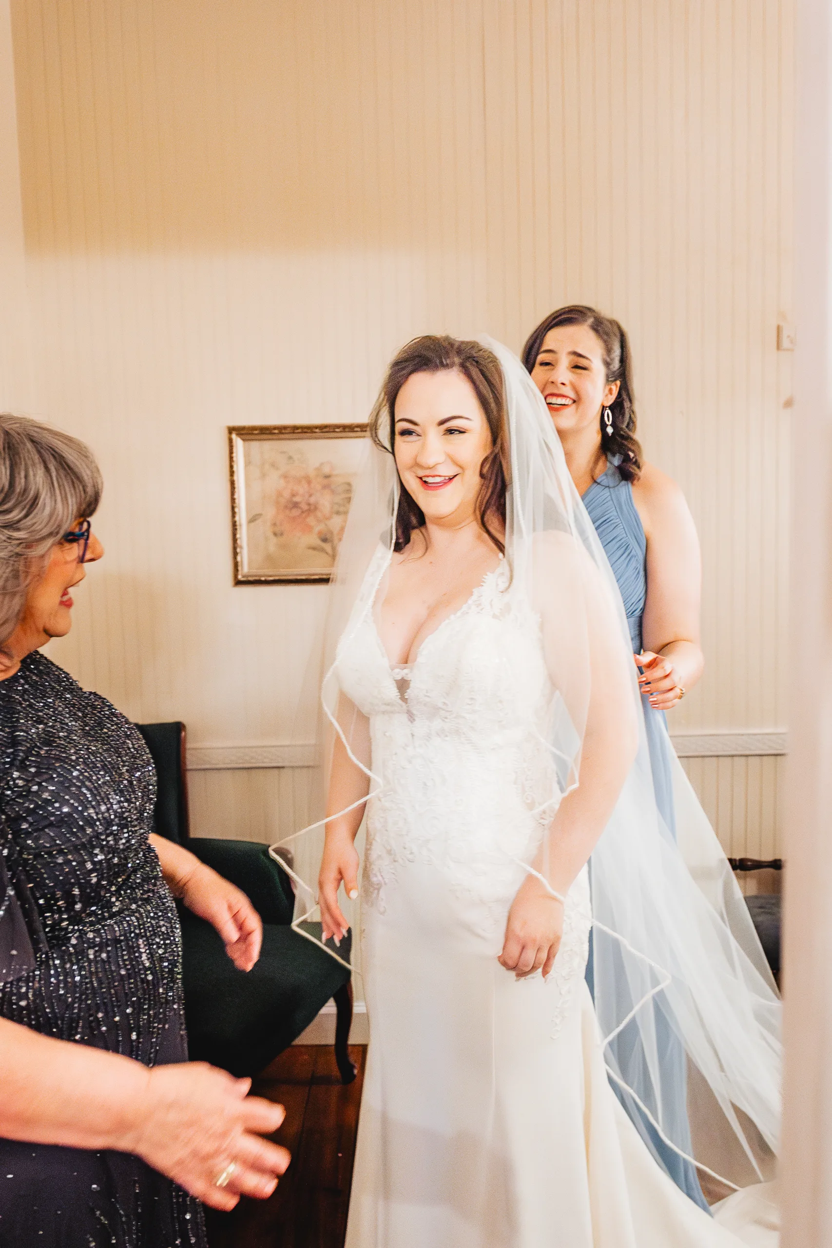 Getting Ready: the bride smiling in her veil with her mom and a bridesmaid before their wedding at Ivy Hall at Roswell Mill in Roswell, GA