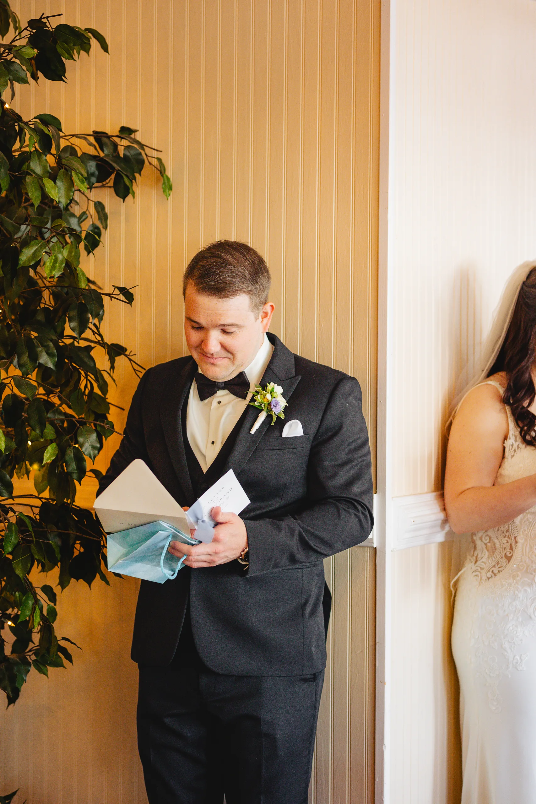 Wedding Details: the groom reading his letter with a gift in his hands at their wedding at Ivy Hall at Roswell Mill in Roswell, GA