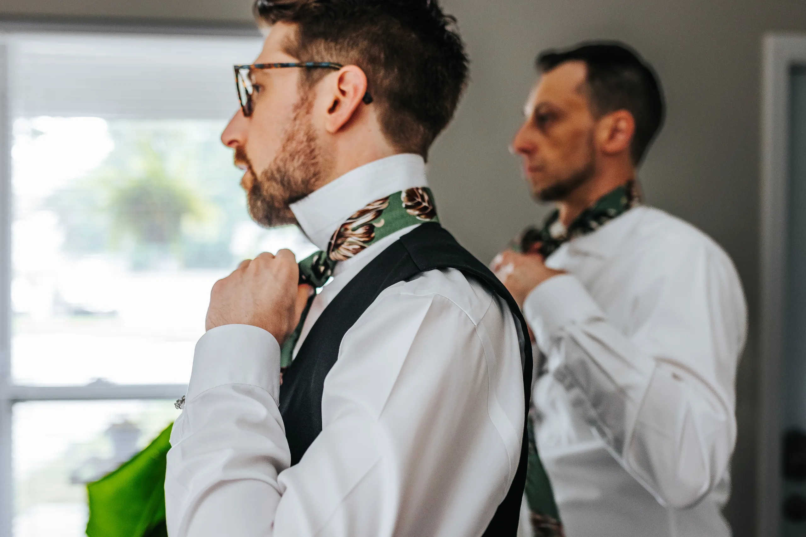 Getting Ready: the groom tying his patterned tie with a groomsman behind him, before their wedding at Terminus 330 in Atlanta, GA