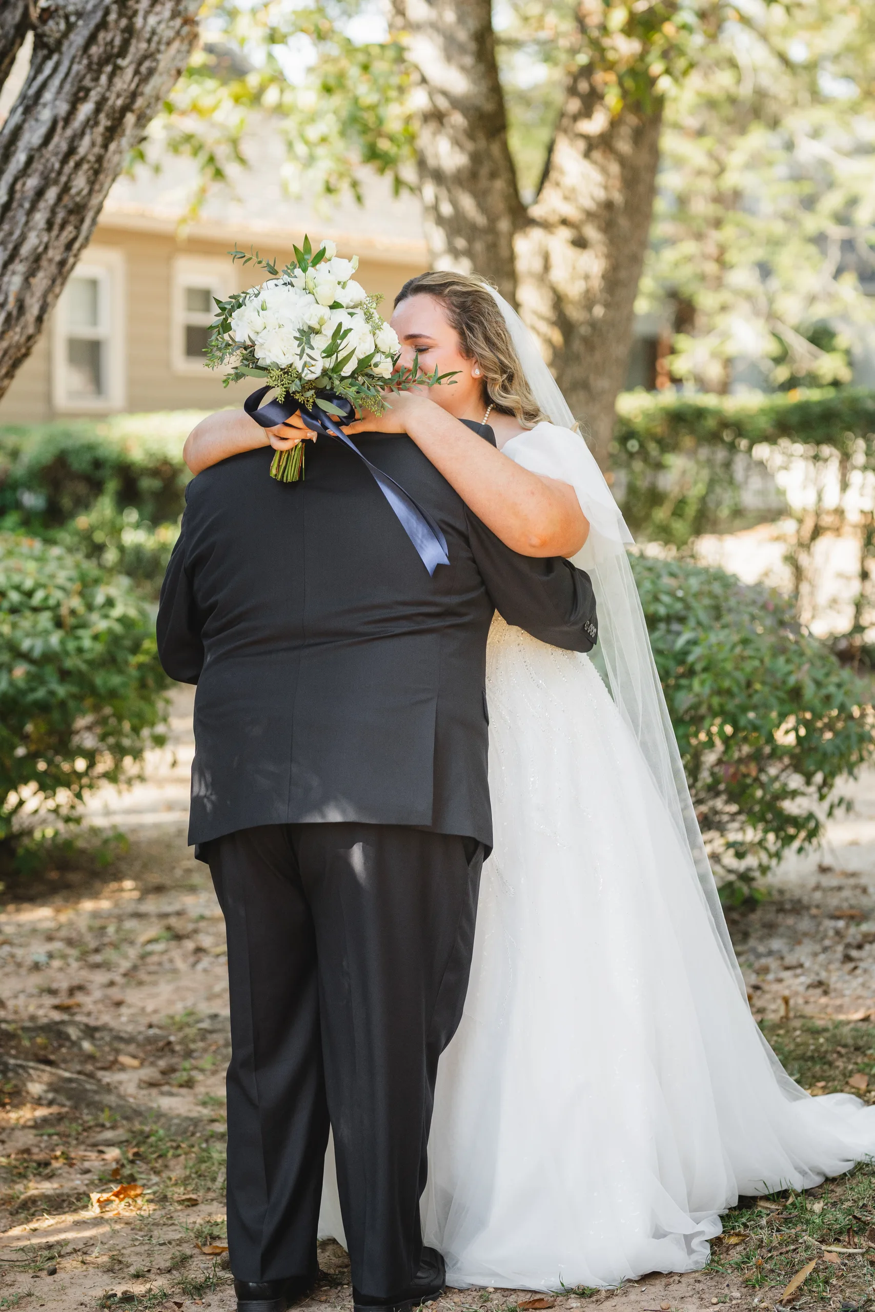 First Look: a hug under the trees, her bouquet over his shoulder, before their wedding at Naylor Hall in Roswell, GA