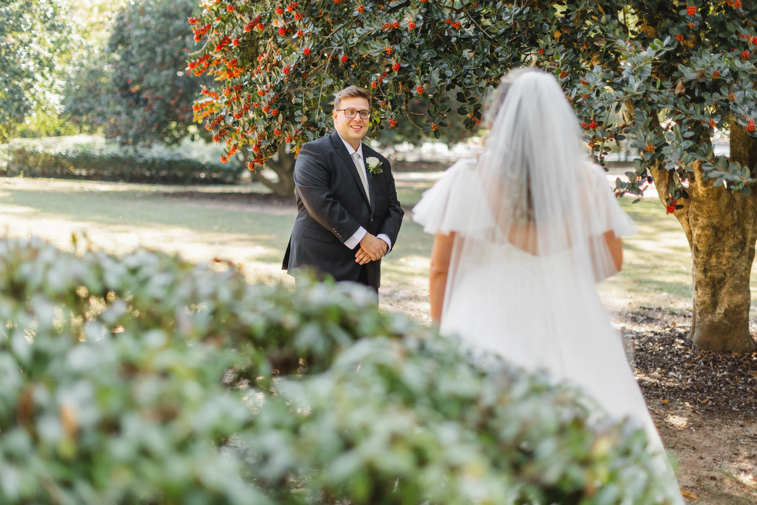First Look: the groom waiting under a flowering tree as she walks up behind him, before their wedding at Naylor Hall in Roswell, GA