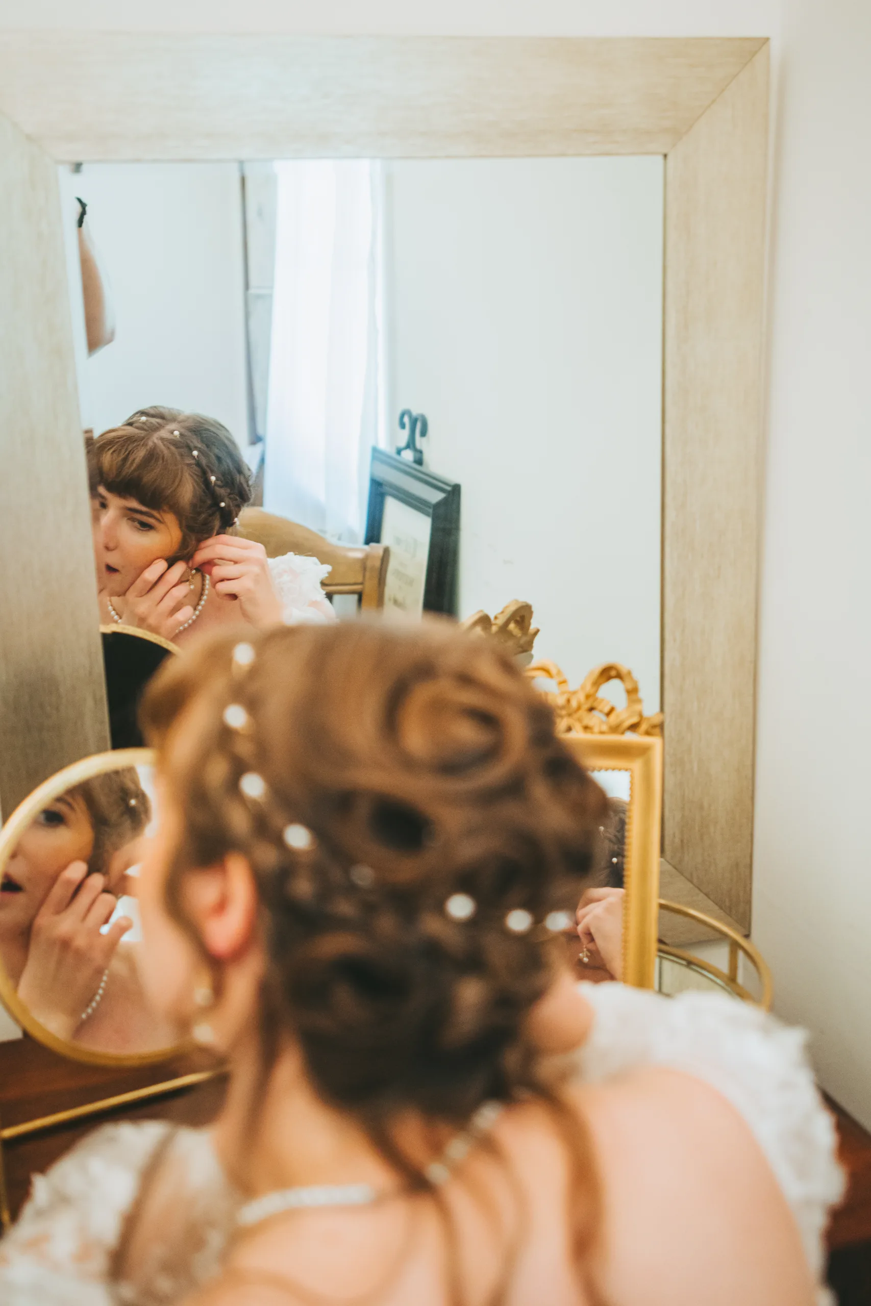 Getting Ready: the bride putting in her earring in the mirror, before their wedding at the Chapel at Simpsonwood Park in Peachtree Corners, GA