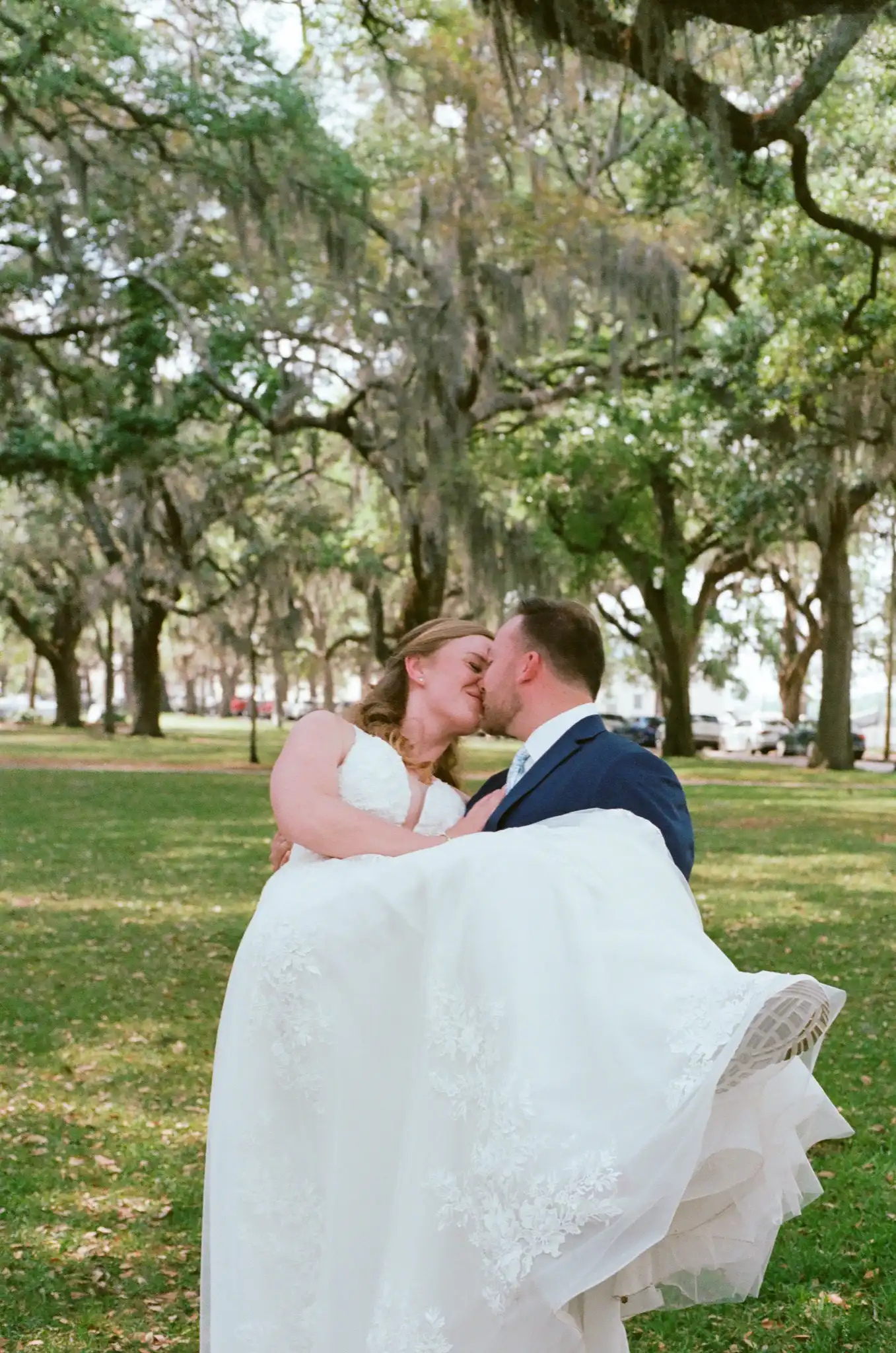 Groom carrying his bride beneath the live oaks and Spanish moss, shot on 35mm film in Savannah, Georgia
