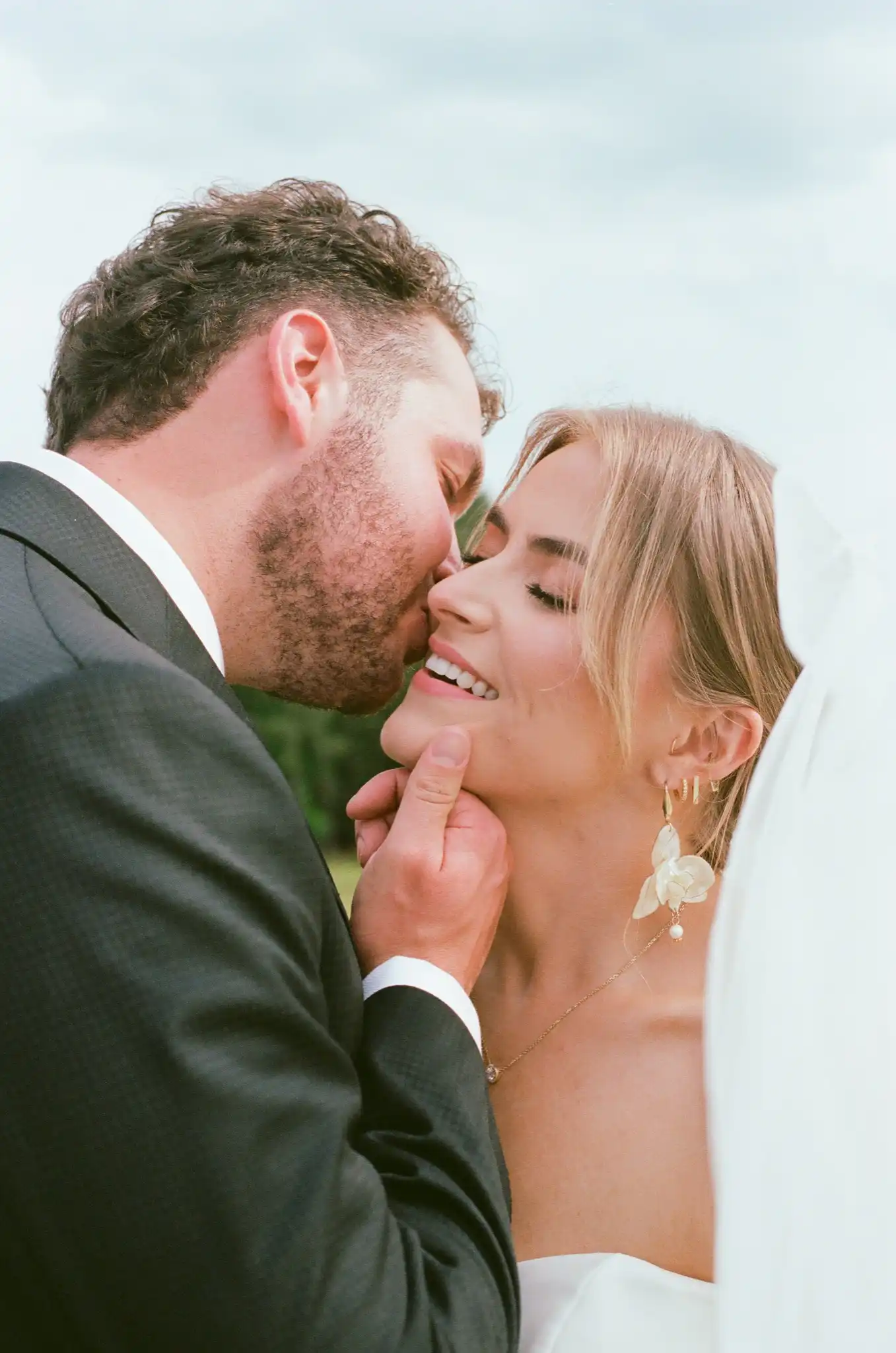 Groom kissing the bride's cheek as she smiles beneath her veil, shot on 35mm film at The Venue at Sharp Mountain in Jasper, Georgia