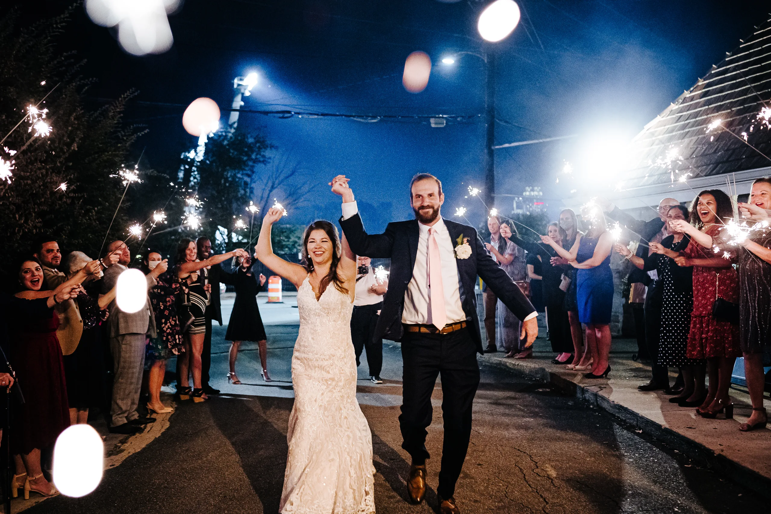Send-Off: their arms up in the air between rows of sparklers, at their wedding at The Piedmont Room in Atlanta, GA