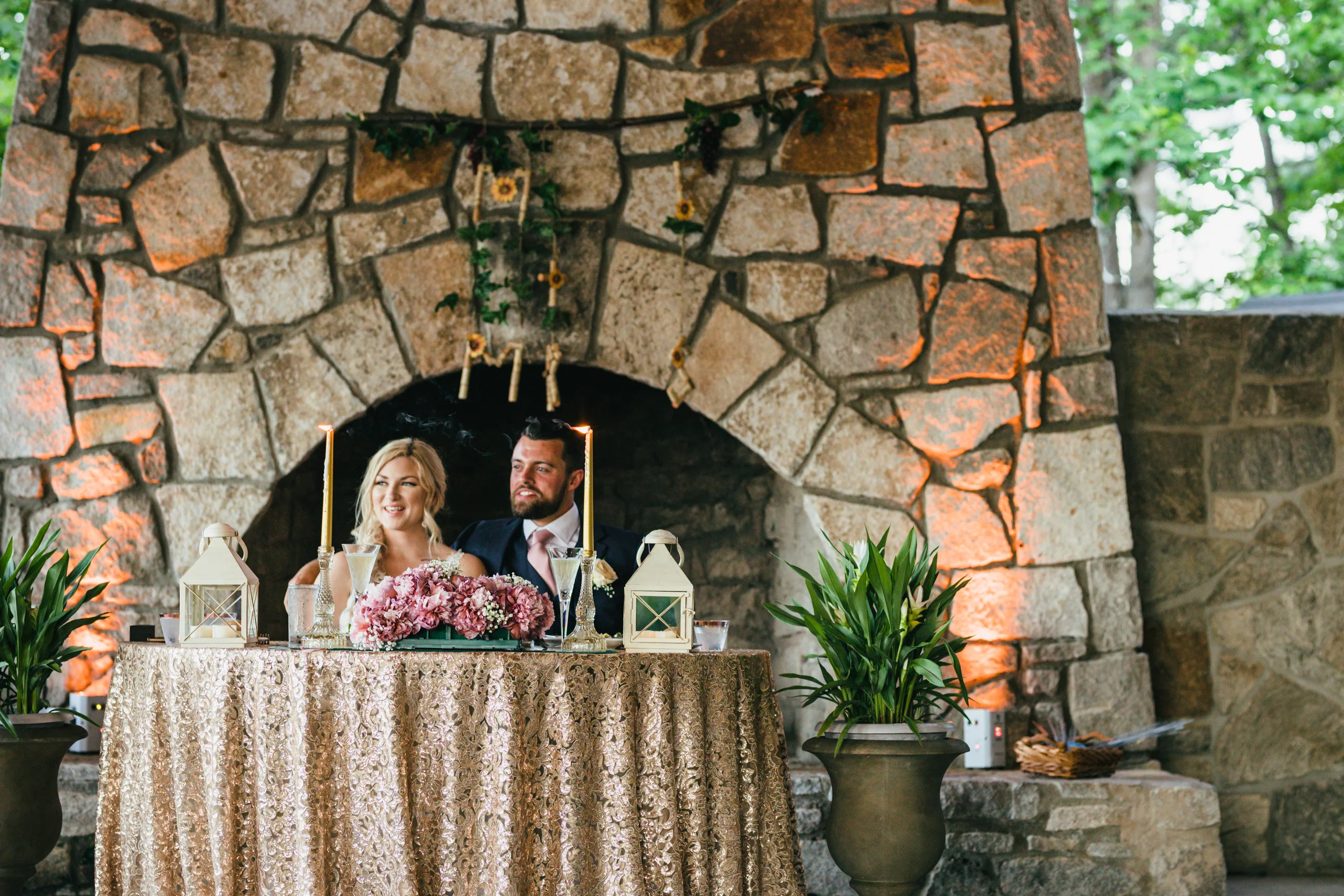 Reception Details: the two of them at the sweetheart table in front of the stone fireplace, at their wedding at Atlanta Evergreen Lakeside Resort in Stone Mountain, GA