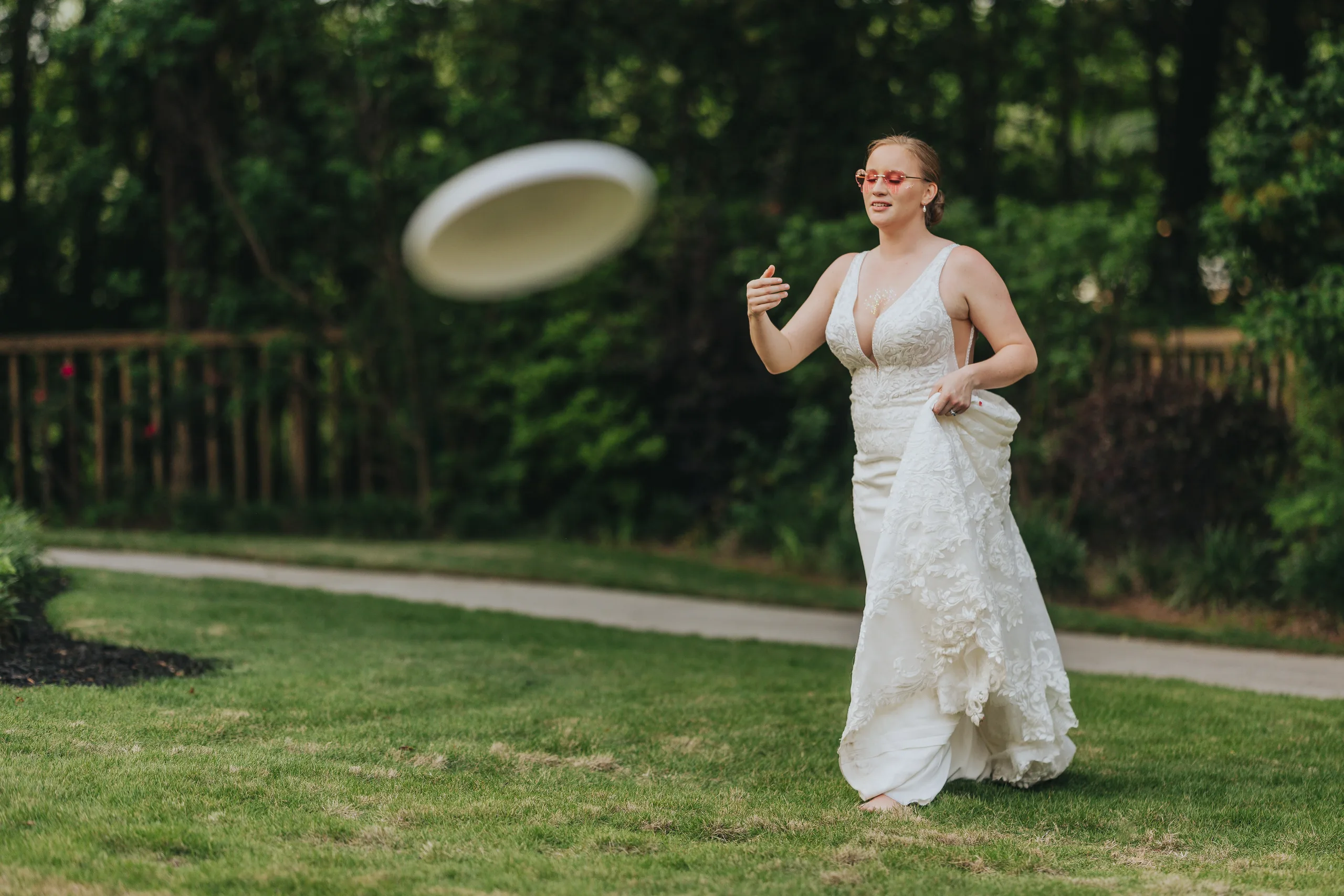 Reception: the bride throwing a frisbee on the lawn in her gown, at their wedding at The Wildflower 301 in Greensboro, GA