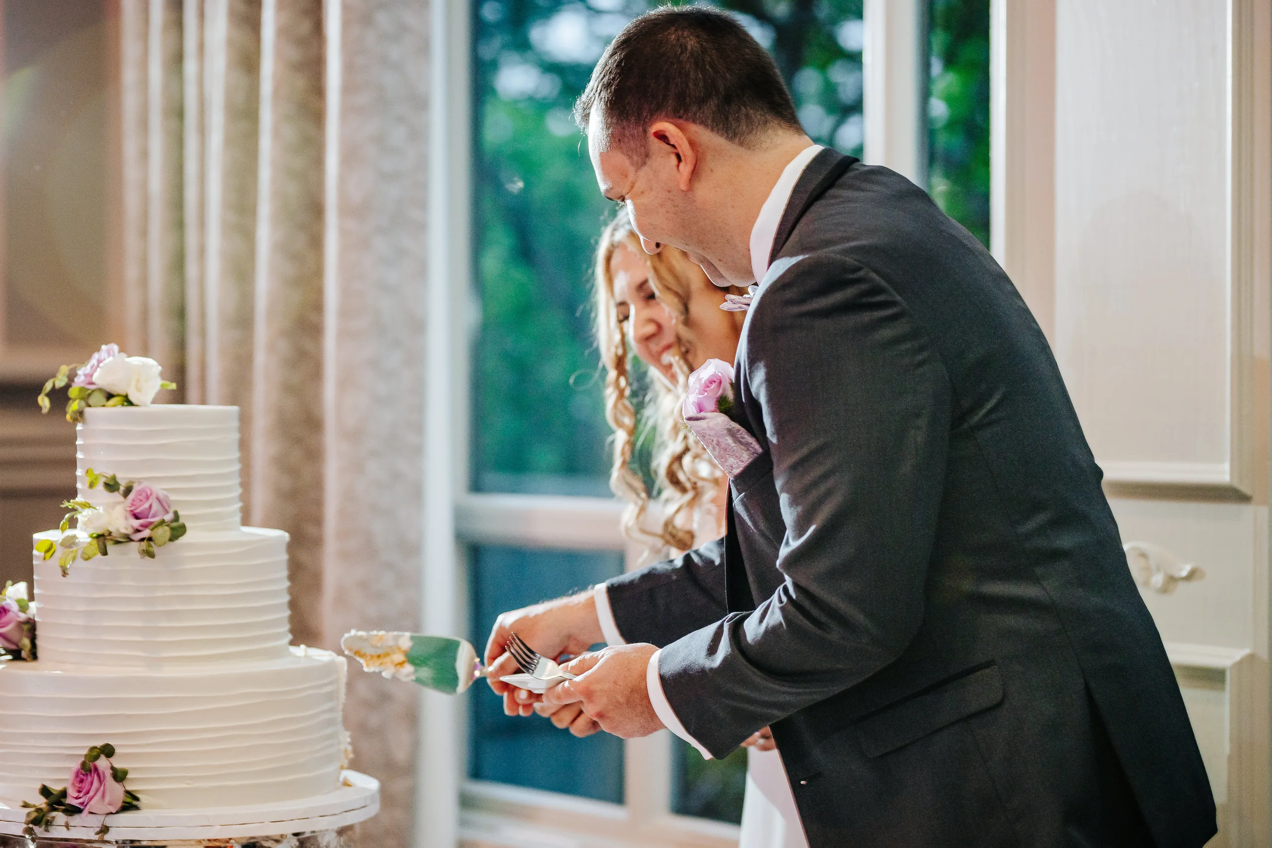 Reception: cutting the cake by the window at their wedding at the Country Club of Roswell in Roswell, GA