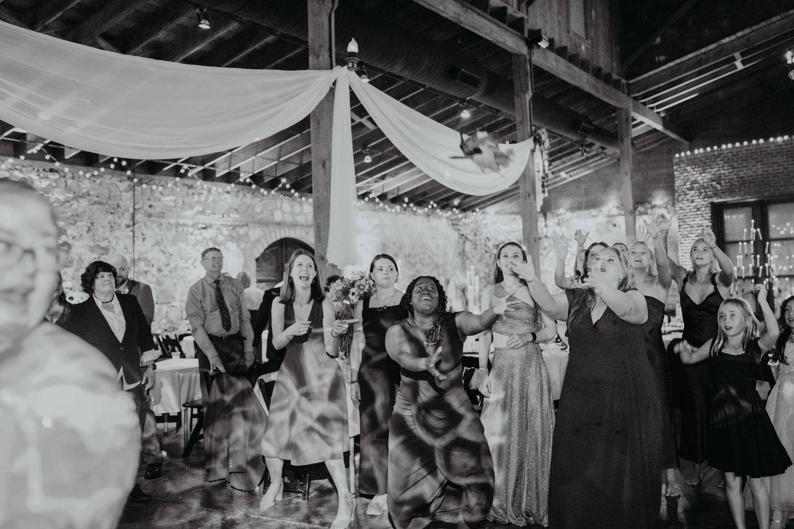 Reception: guests waiting for the bouquet toss, in black and white, at their wedding at 550 Trackside in Lawrenceville, GA