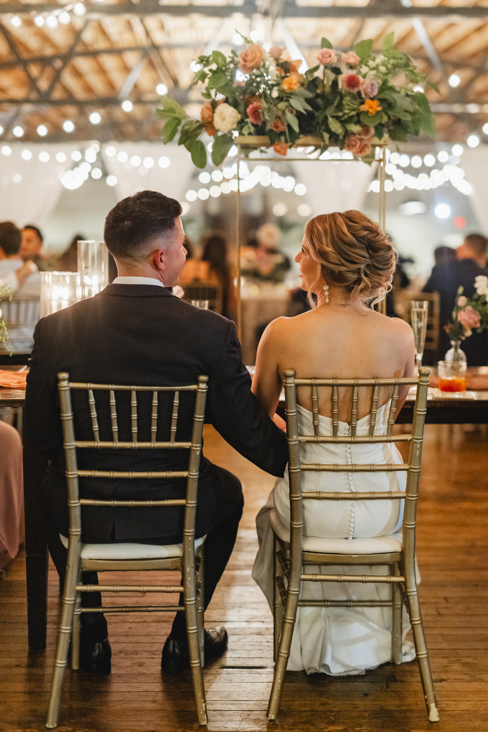 Wedding Reception: the two of them at the sweetheart table under a suspended floral arrangement, at their wedding at Summerour Studio in Atlanta, GA