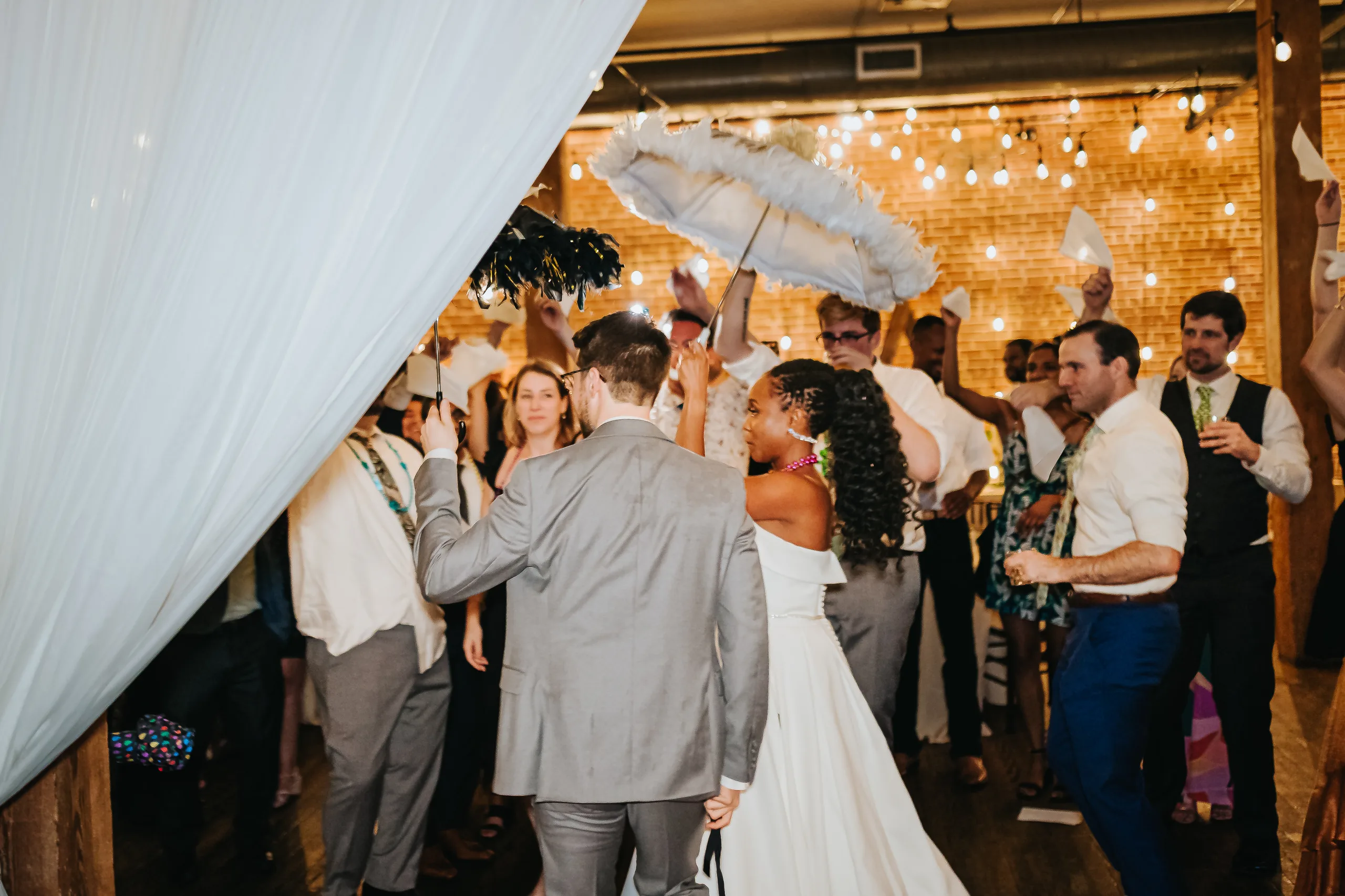 Reception: guests following the second line with parasols and handkerchiefs, at their wedding at Terminus 330 in Atlanta, GA