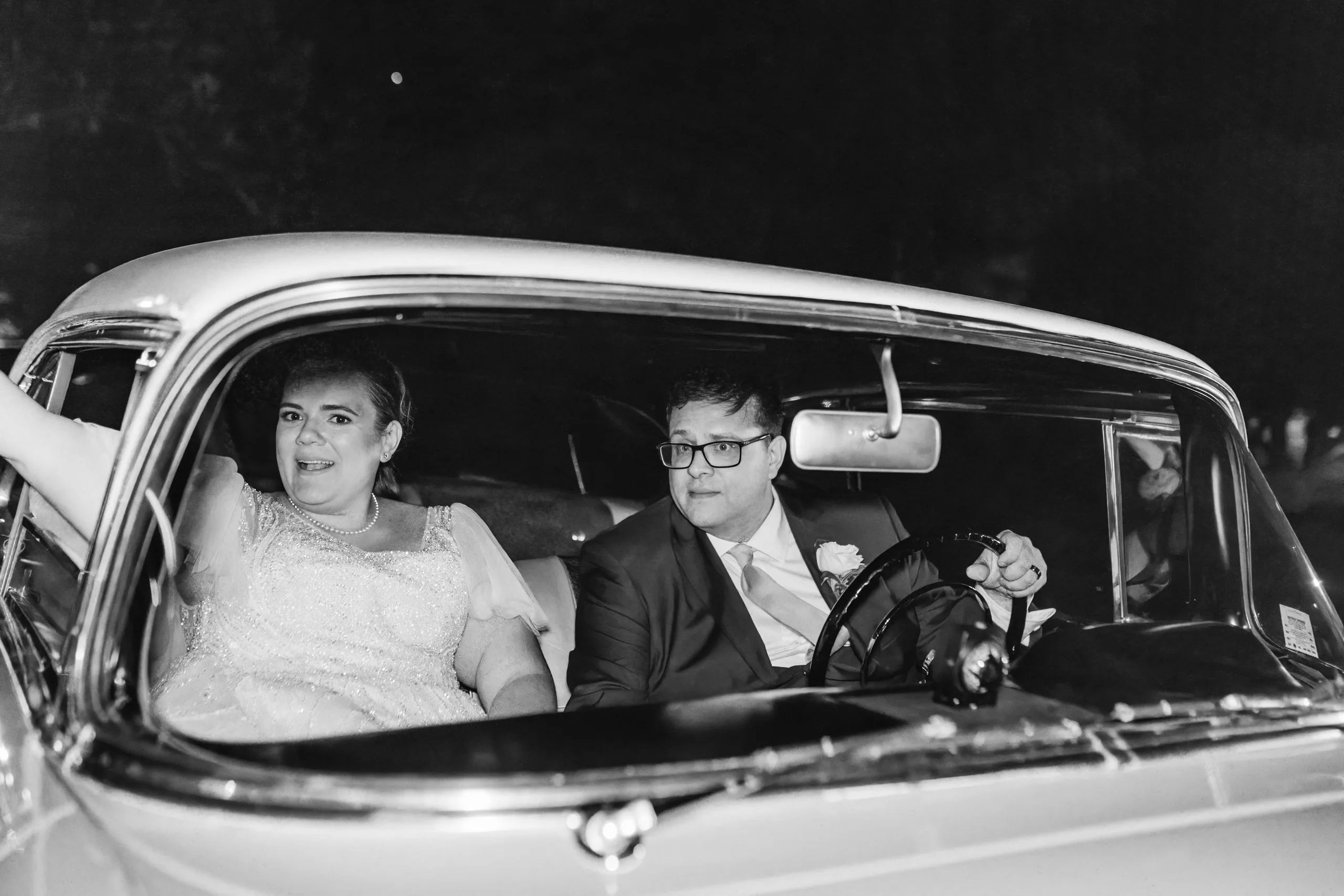 Send-Off: waving from the Chevrolet as they drive off, in black and white, at their wedding at Naylor Hall in Roswell, GA