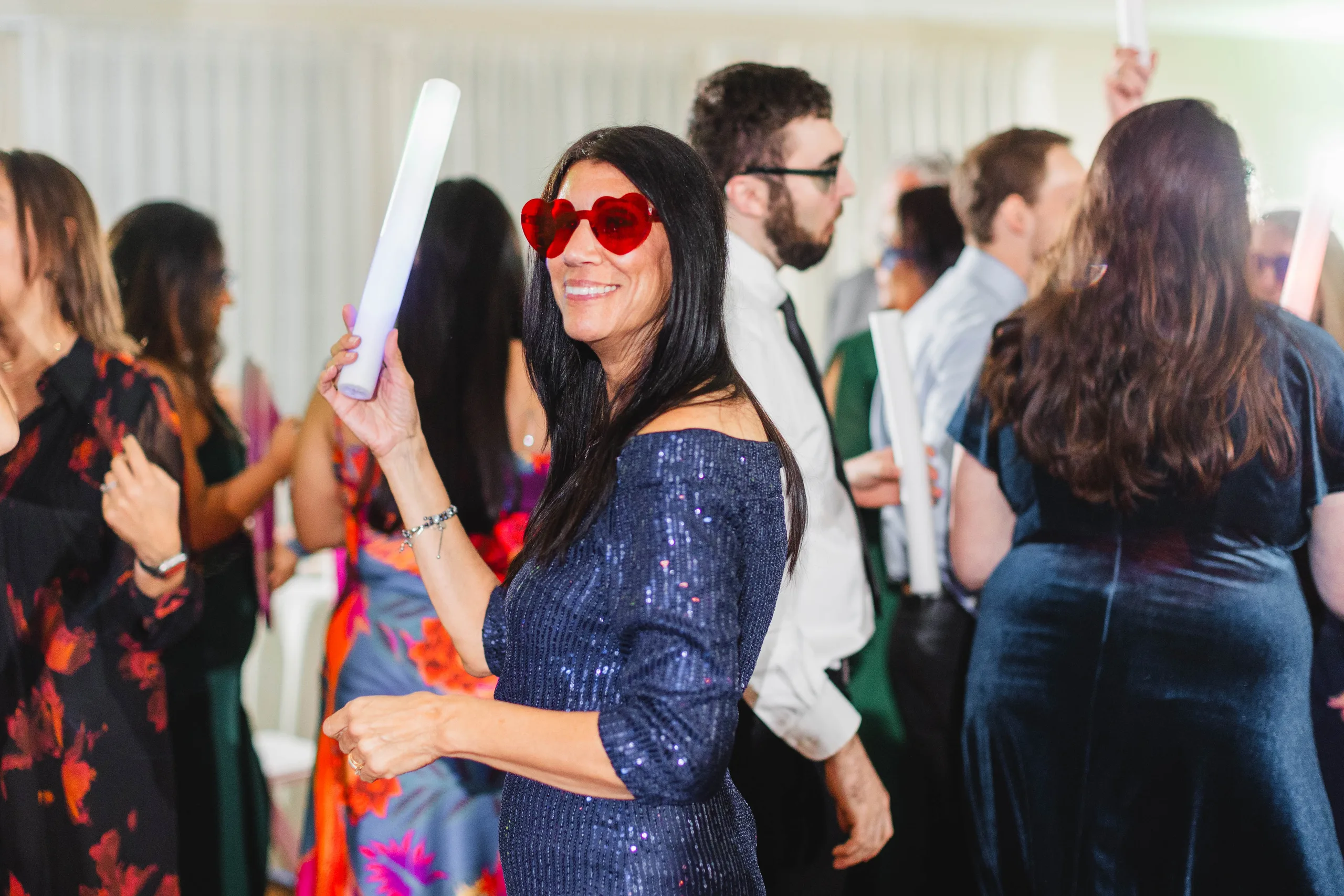 Reception: a guest in heart sunglasses dancing with a light-up wand, at their wedding at Naylor Hall in Roswell, GA