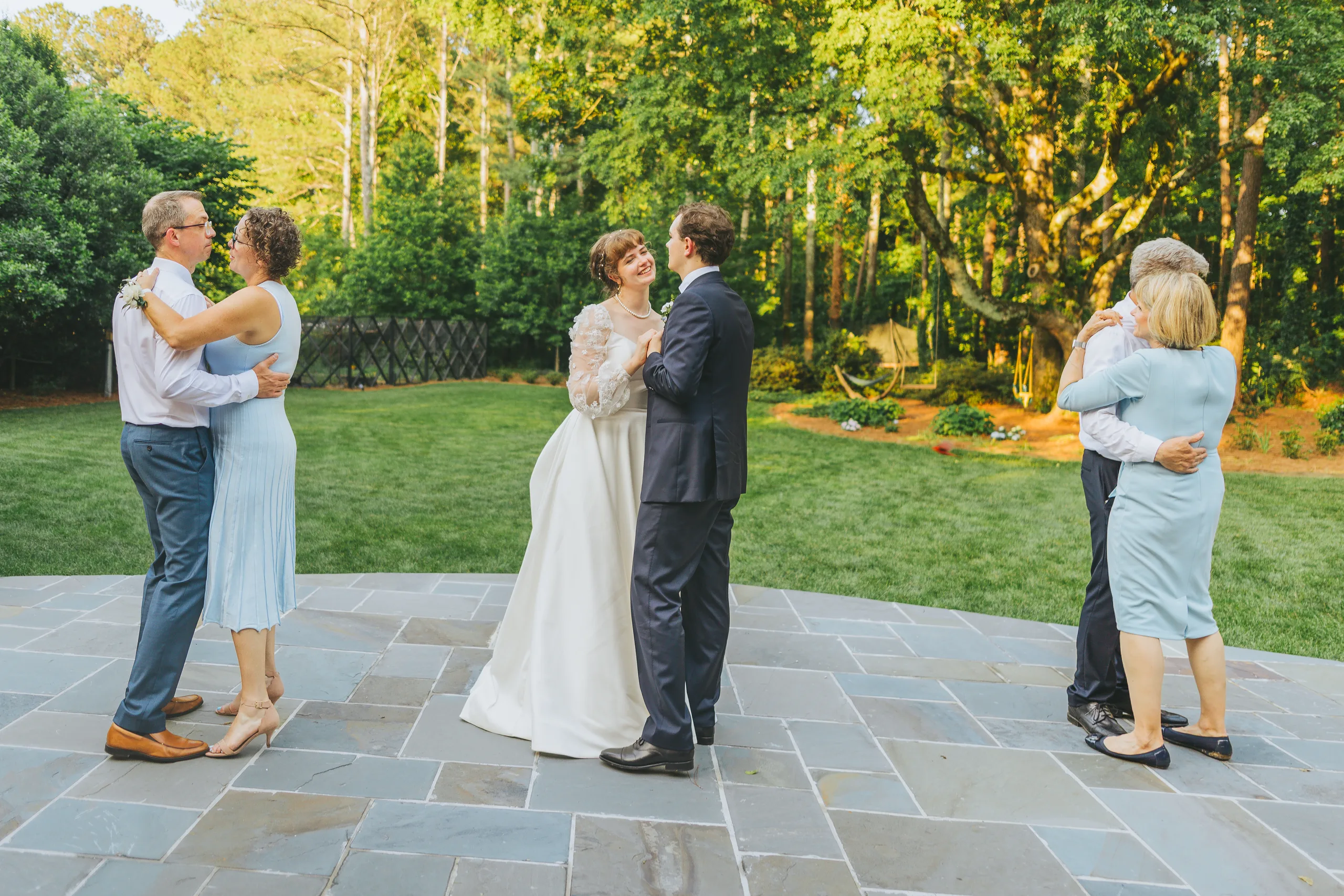 Reception: dancing with their parents on the patio, at their wedding reception at a family home