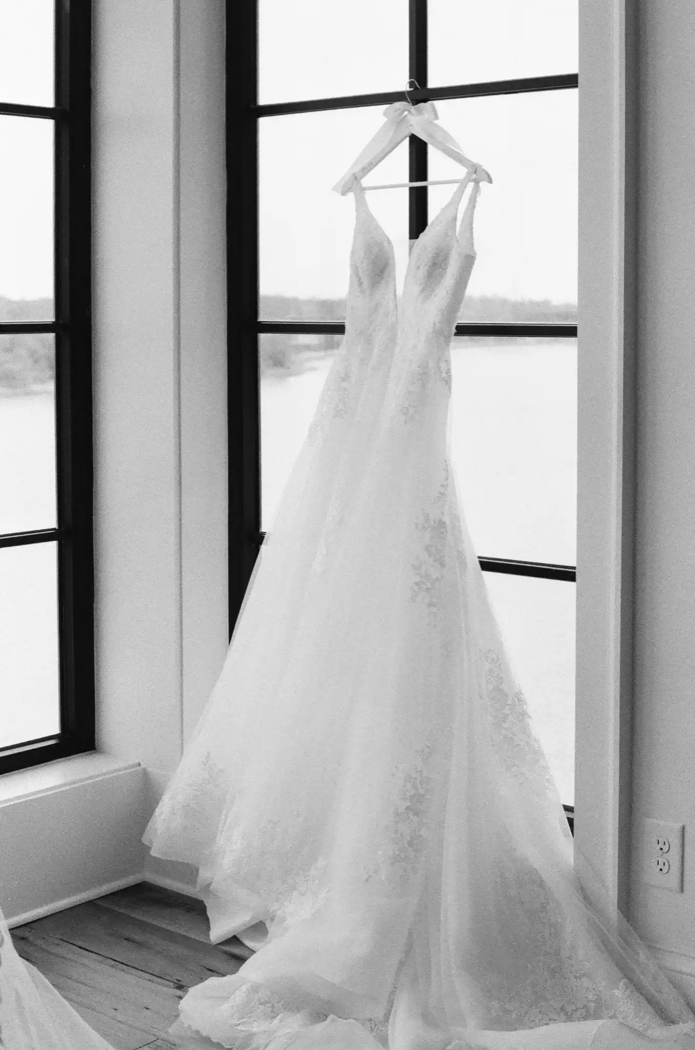 Lace wedding gown hanging in a window overlooking the river, in black and white on 35mm film at a private riverfront residence in Savannah, Georgia
