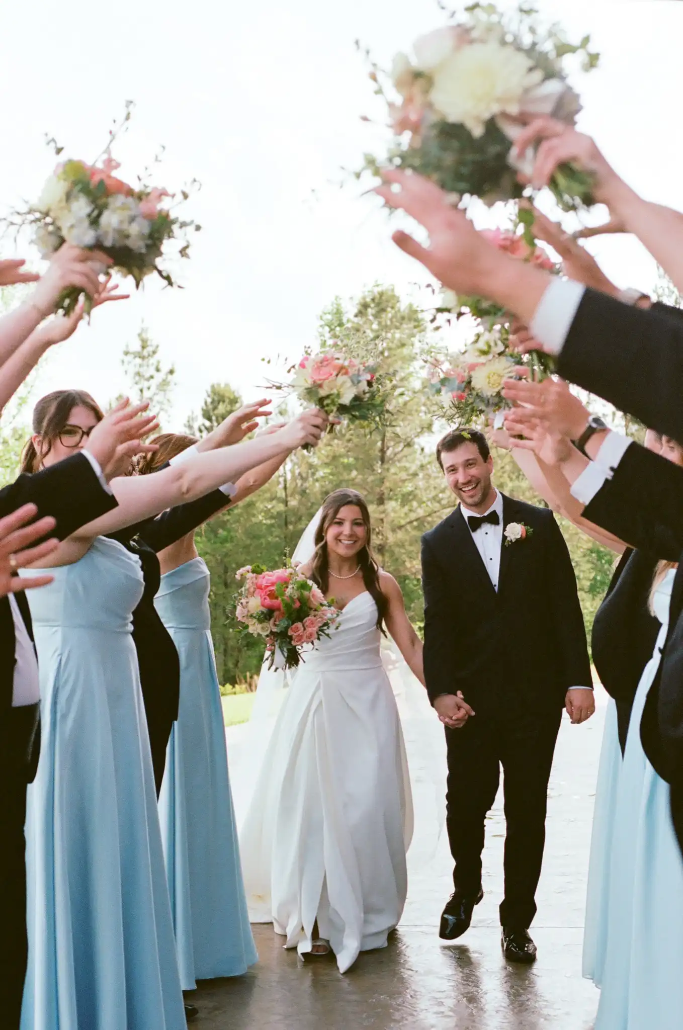 Bride and groom walking through a tunnel of raised bouquets after the ceremony, shot on 35mm film at The Venue at Sharp Mountain in Jasper, Georgia