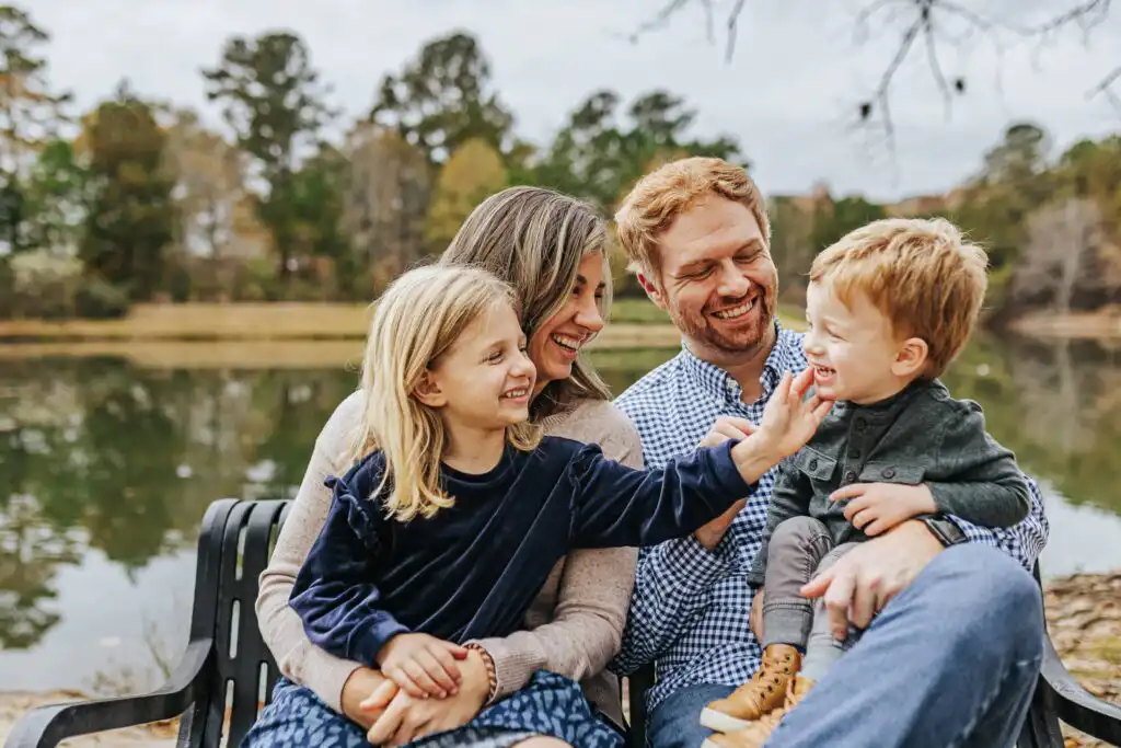 Family seated on a dock beside a lake in autumn during a family portrait session