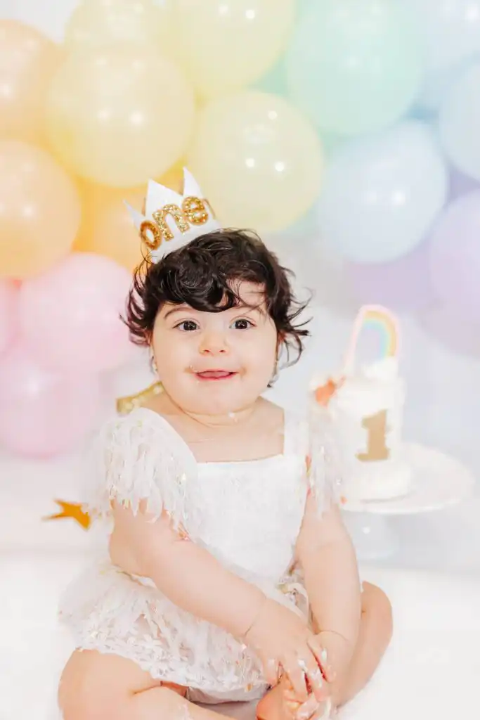 First birthday cake smash session with pastel balloons and a one year old in a crown