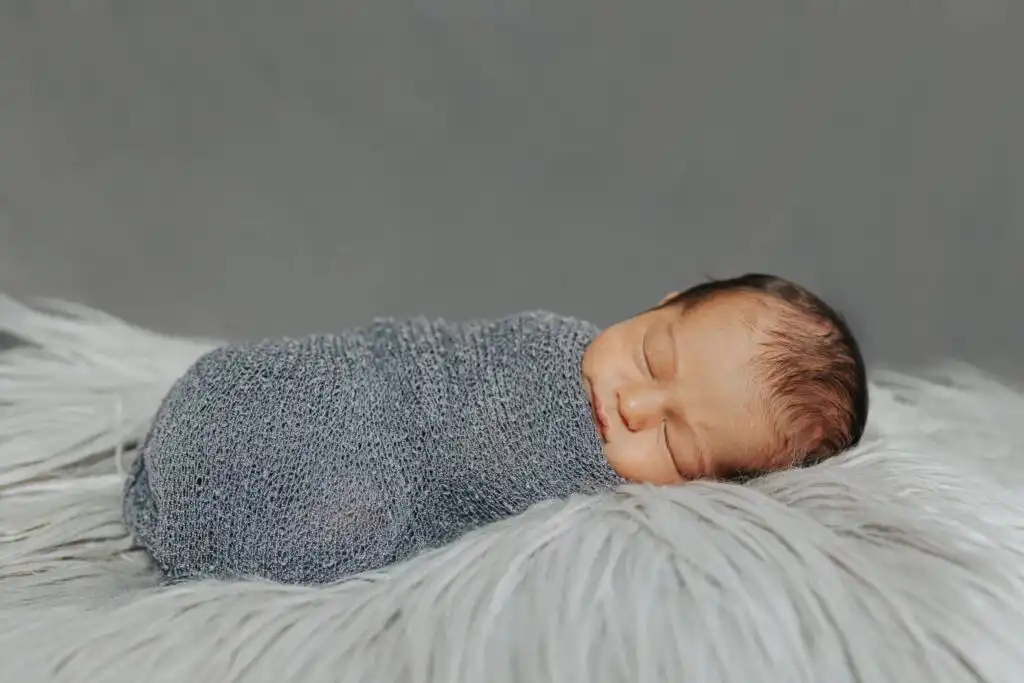 Sleeping newborn wrapped in a grey swaddle on soft fur during a newborn session